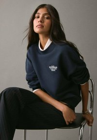 Námořnická mikina s bílým nápisem "BOHEMIAN Country Side SOUL", žebrovaným výstřihem a mírně oversized střihem, kombinovaná s pruhovanými kalhotami.