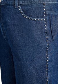 Temno modri jeans iz denima z srebrnimi žebljički ob žepih in stranskih šivih za dodatno podrobnost. Klasična zasnova s petimi žepi.