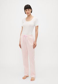 Vit kortärmad topp kombinerad med rosa randiga pyjamasbyxor som har dragsko i midjan. Mjuk tyg med en avslappnad passform.