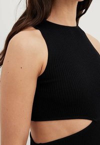 Top court noir à côtes avec un col haut, présentant une découpe sur le côté. Il dispose d'un design ajusté et d'une surface texturée.