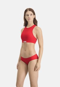 Rotes Sport-Crop-Top und passende Bikinihose, beide aus elastischem Material gefertigt. Das Top verfügt über ein Logo am Bündchen und einen hohen Halsausschnitt.