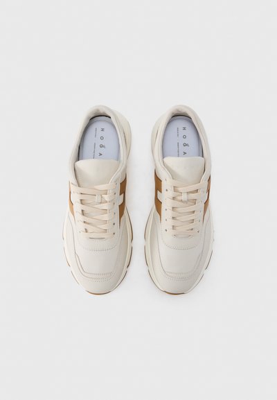 Μπεζ αθλητικά παπούτσια με υφή στην επάνω επιφάνεια, καφέ πλευρικές ρίγες, στρογγυλεμένη μύτη και επίπεδα κορδόνια. Διαθέτουν μαλακή σόλα για άνεση.