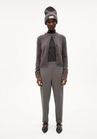 Grijze gebreide cardigan met knopen, gestreepte coltrui, grijze broek en oversized grijze beanie. Zwarte puntige schoenen met enkelriemen.