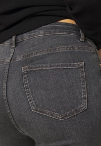 Mörkgrå jeans i denim med en klassisk femficksdesign, kontrasterande sömmar och en slät, texturerad yta.