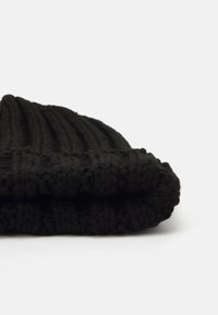 Black knitted beanie, featuring a ribbed texture and a fold-over cuff. Soft yarn with visible stitches and a smooth, thick fabric.