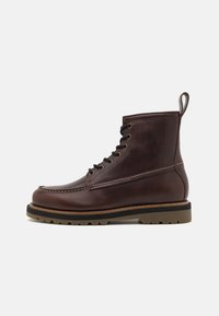 Brune lær snøreboter med et midhøyt design, rund tå, solid gummisåle og sømdetaljer langs tåen og siden.