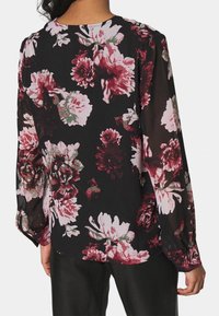 Bloemrijke blouse van doorschijnende zwarte stof met grote roze en bordeauxrode bloemen, lange mouwen met gathered cuffs en ronde halslijn.