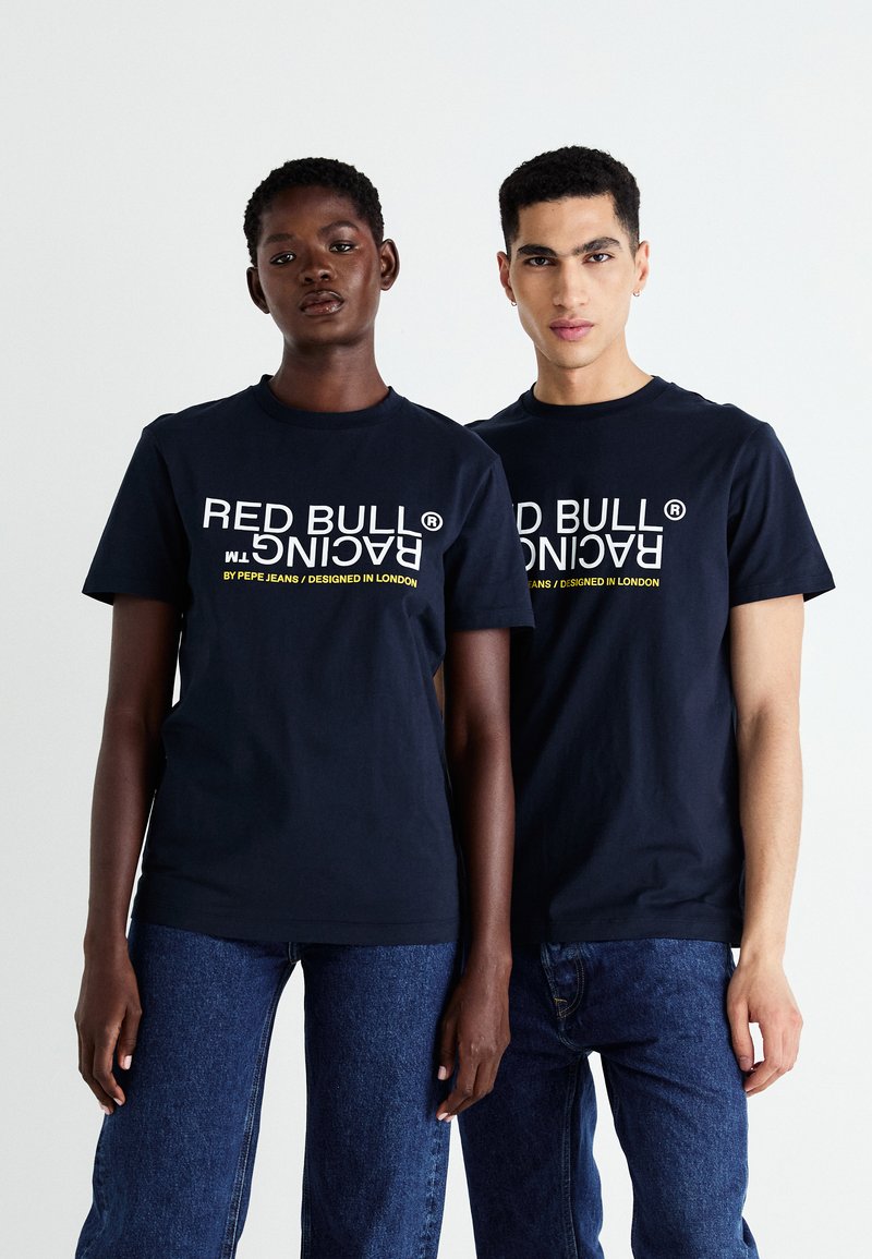 Marineblå bomulds t-shirts med "RED BULL RACING" og mærkedetaljer i hvid og gul tekst, der er parret med blå denimjeans.