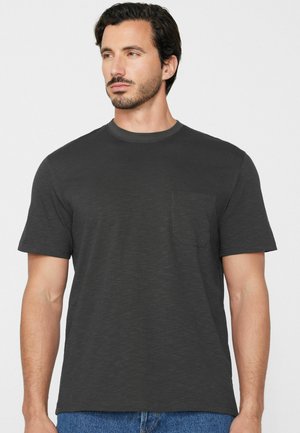 Homme aux cheveux courts et foncés portant un t-shirt gris foncé à manches courtes avec un col rond et une poche poitrine.
