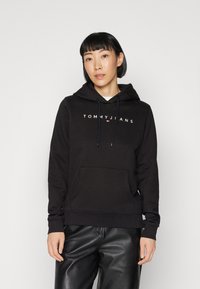 Sudadera negra de mezcla de algodón, con bolsillo frontal, capucha con cordón y logo blanco "TOMMY JEANS". Textura suave, ajuste casual.