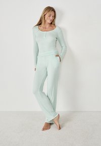 Mintgroene geribbelde pyjamastel met lange mouwen en een ronde hals. De broek heeft een losse pasvorm en gerimpelde onderranden. Zachte textuur, casual ontwerp.