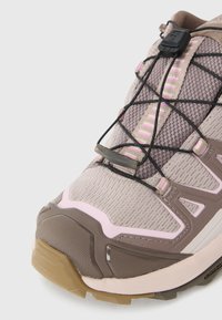 Lichte wandelschoen met een beige mesh bovenwerk, roze accenten, een elastisch vetersysteem en een getextureerde bruine rubberen zool voor grip.