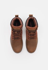 Bruine leren enkellaarsjes met zwarte accenten en beige veters. Voorzien van een gevoerde kraag, een trekloop, en een gestructureeerde rubberen zool.