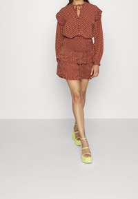 Rotes gemustertes Zweiteiler-Outfit mit Rüschebluse und passendem Rock. Getragen mit limettengrünen Plateauschuhen mit Knöchelriemen.