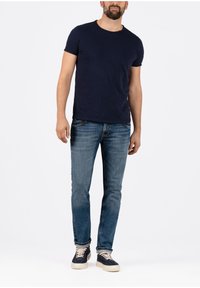 Navy-blaues kurzärmeliges T-Shirt kombiniert mit ausgewaschenen blauen Jeans und marineblauen Sneakern mit cremefarbenen Schnürsenkeln, die einen lässigen, entspannten Look präsentieren.
