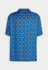Chemise bleue à manches courtes avec un col pointu, présentant un motif floral et géométrique répétitif en rouge, blanc et vert.