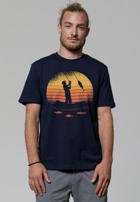 T-shirt bleu marine en coton avec un pêcheur, un coucher de soleil orange et des graphiques stylisés de poisson. Manches courtes et design col rond.