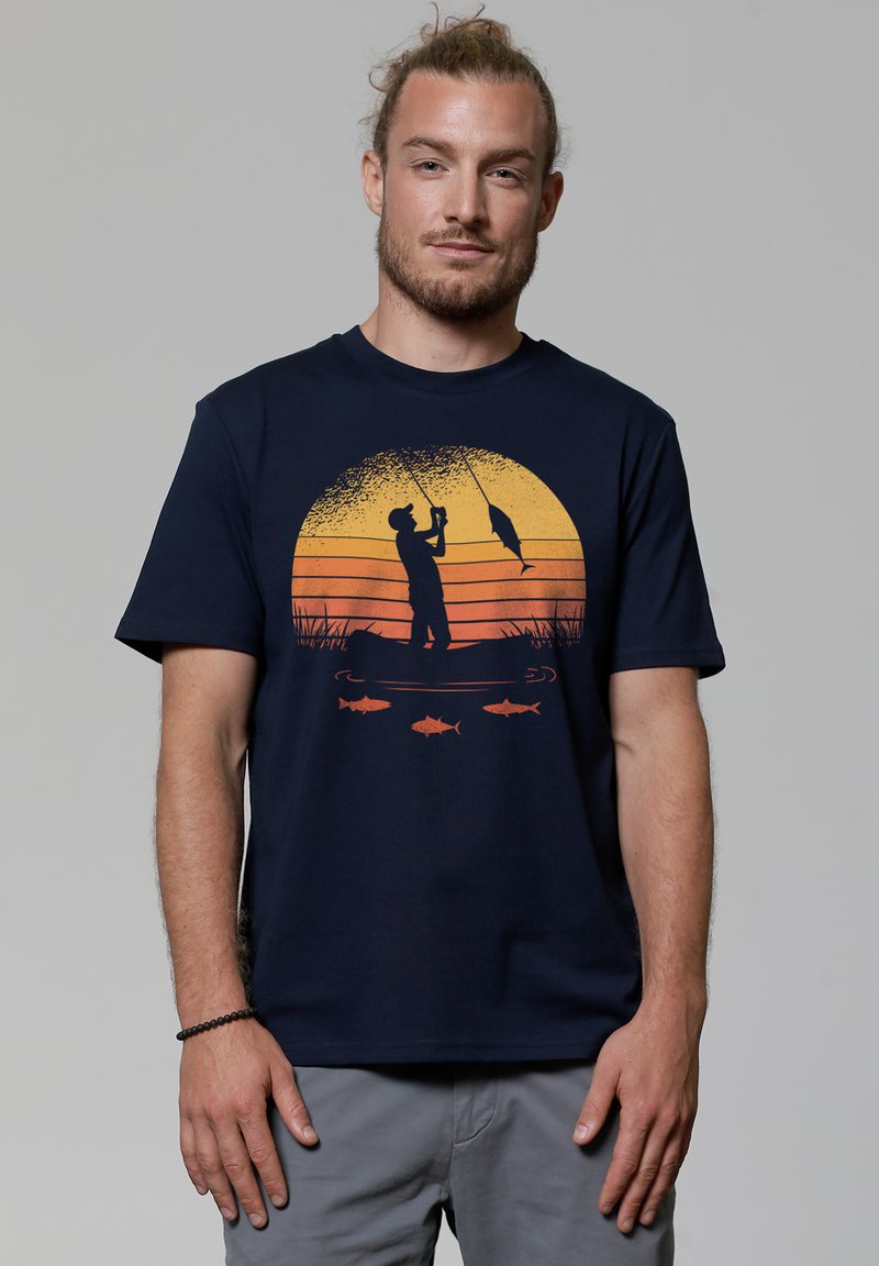 T-shirt bleu marine en coton avec un pêcheur, un coucher de soleil orange et des graphiques stylisés de poisson. Manches courtes et design col rond.