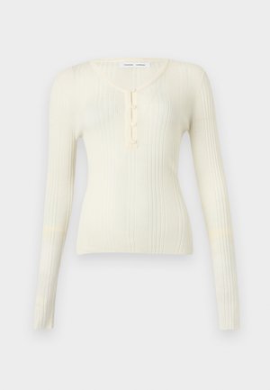 Hosszú ujjú bordázott kötött felső halványsárga színben, V-nyakkivágással és három gombos gombolással. Fitt fazonú és lágy tapintású.