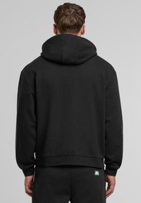 Schwarzer Kapuzenpullover mit langen Ärmeln und einem lockeren Schnitt. Mit einem gerippten Saum und Bündchen gefertigt aus weichem, dickem Stoff.