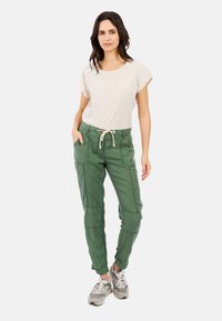 Licht beige gestructureerde top met korte mouwen, gecombineerd met groene cargobroek met zakken, een trekkoord in de taille en gestikte details. Gekozen voor grijze sneakers.