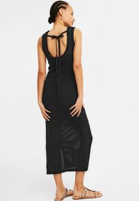 Robe noire en crochet présentant une fermeture à lien dans le dos, un design sans manches et une longueur arrivant au genou avec un motif texturé.