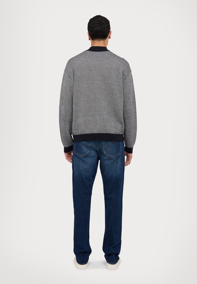 Pullover a maglia nera e bianca a righe con una texture, maniche e colletto a coste, abbinato a jeans in denim blu scuro.