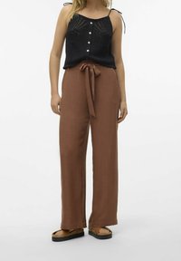 Top en tricot noir sans manches avec des détails de boutons et un pantalon large marron doté d'une taille nouée. Modèle portant des sandales marron.