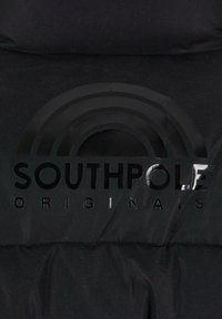 Sort puffer-jakke materiale med en blank sort logo med teksten "SOUTHPole" og et regnbuegrafik ovenfor. Tekstureret overflade.
