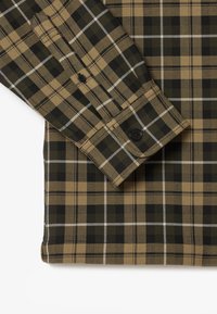 Brun och grön rutig skjorta med knäppta ärmslut, som har svarta, vita och tan linjer, samt en strukturerad tyg.