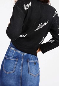 Černý pletený svetr s bílým nápisem "Icon", kombinovaný s modrou džínovou sukní se dvěma kapsami a trojúhelníkovým detailem loga.