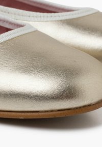 Ballerine metalliche dorate con superficie texturizzata, bordi bianchi e interno morbido rosa. Presentano una punta arrotondata e una suola naturale.