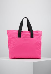 Růžová taška na rameno s černými textilními držadly, obdélníkového tvaru, vyrobená z odolného materiálu, s jednoduchým designem a boční kapsou.