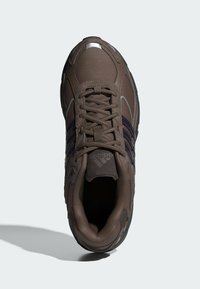 Brun athletisk sko med andningsbart mesh-övre, lila ränder och texturerad gummisula. Har reflekterande detaljer och förstärkt tåhätta.