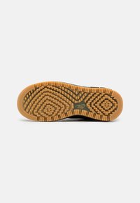 Semelle en caoutchouc d'une chaussure noire avec un motif de bande de roulement présentant des formes géométriques et le logo Nike sur fond blanc.