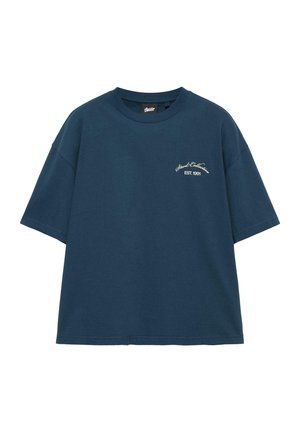 Tmavomodré oversized tričko s krátkym rukávom s malým bielym textom "Stud Collection EST. 1991" na ľavej strane hrude.