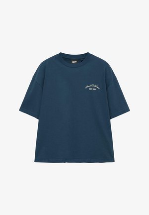 Marineblaues oversized T-Shirt mit kurzen Ärmeln und kleinem weißem Schriftzug „Stud Collection EST. 1991“ auf der linken Brust.