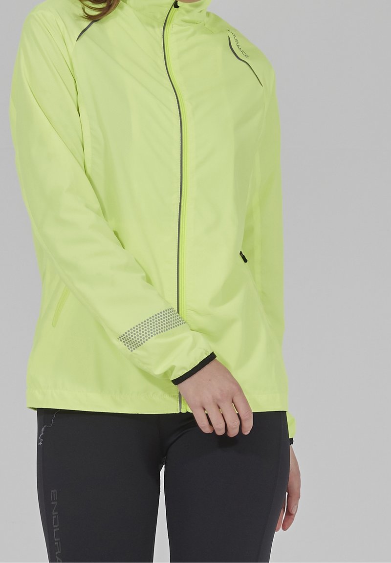 Fluorescenční žlutá bunda s vysokým límcem, předním zipem a reflexními detaily. Obsahuje síťovinu na rukávech a voděodolný materiál.
