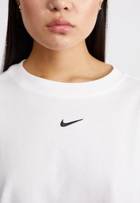 Fehér pamut póló kerek nyakkivágással, kisebb fekete Nike swoosh logóval a mellkason. Simává és kényelmes egyedi dizájn.