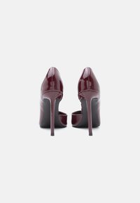 Burgundy patent leather high-heeled shoes with a sleek design, pointed toe, and open back. Thin, high stiletto heels.