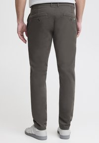 Chinos slim fit verde scuro con tasche posteriori, dettagli in bottone e una texture liscia, abbinati a scarpe da ginnastica grigie.