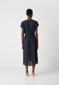 Navy blue, polka dot midi dress with short sleeves and a drawstring waist. Lightweight fabric, sheer layering at hem. Worn with beige heels.