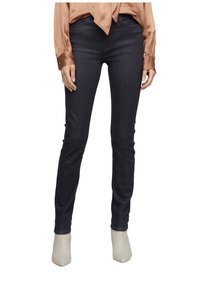 Vaqueros skinny de un azul oscuro, hechos de denim, con una cintura de altura media y detalles de costura mínimos, combinados con botas de tacón en color crema.