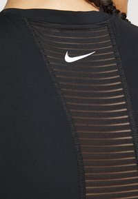 Sort atletisk top med gennemsigtig stribet ryg, med et lille hvidt Nike-logo over halsudskæringen og kontrastfarvet syning langs sømmene.