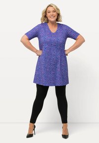 Vestido corto morado de manga corta con un patrón floral, escote en V y silueta fluida, combinado con leggins negros y tacones.