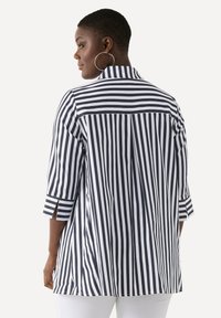 Maglietta a righe navy e bianche con colletto, maniche a tre quarti e spacchi laterali. Tessuto morbido e design dalla vestibilità comoda.