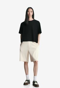 Črn, oversized T-shirt s kratkimi rokavi, v kombinaciji s bež, nabrano krilo. Bele nogavice in črno-bešične čevlje dopolnjujejo obleko.