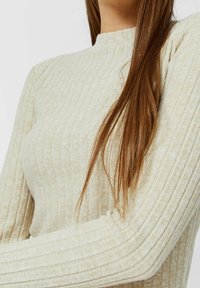 Top a maniche lunghe lavorato a costine beige. Caratterizzato da un colletto alto e un design attillato, evidenzia una texture morbida con sottili linee orizzontali.