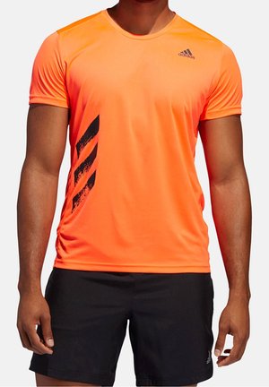 Homme portant un t-shirt Adidas à manches courtes orange vif avec des rayures diagonales noires et un short Adidas noir.
