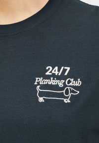 Donkerblauwe t-shirt van katoen met een ronde hals. Voorzien van witte borduurwerk van "24/7 Planking Club" en een lijntekening van een teckel.